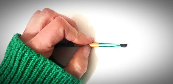 Close-up of hand holding pencils against white background