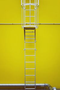 Metallic ladder against yellow wall