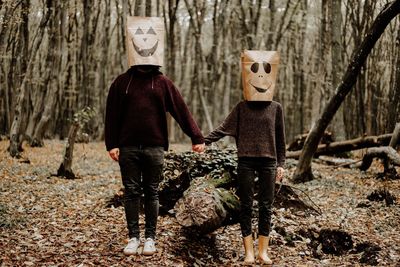 Rear view of friends standing by tree trunk in forest in halloween day