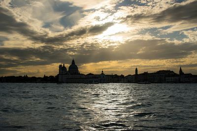 City at waterfront against cloudy sky