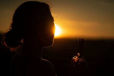 Close-up of woman holding glass bottle during sunset