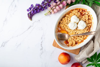 Fresh homemade nectarine crumble with vanilla ice cream in ceramic form on white marble background