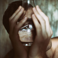 Close-up of man looking through glass bottle