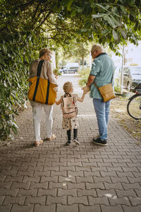 Grandparents holding hands of granddaughter while walking on footpath