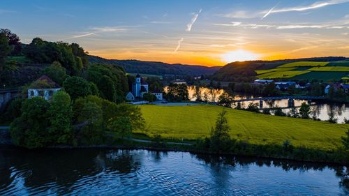 Scenic view of river by buildings against sky at sunset