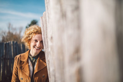 Portrait of smiling young woman standing against a fence