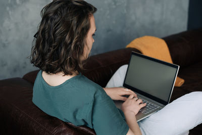 Young woman working from home with laptop, showcasing blank screen mock-up