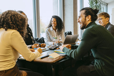 Cheerful students talking while sitting at table in cafeteria