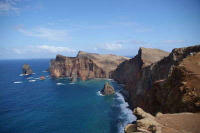 Scenic view of rocky mountains at sea shore against sky