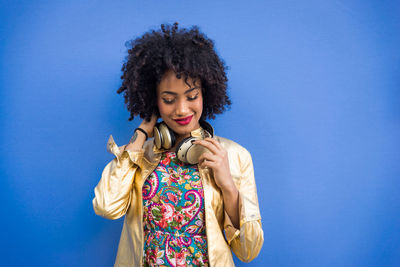 Fashionable young woman with curly hair against blue background