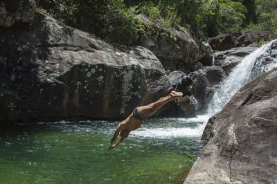 Shirtless man jumping in stream