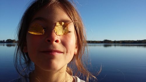 Close-up of teenage girl covering eyes with autumn leaves against lake
