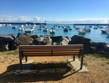 Rear view of empty bench in sailboats harbor in sea against blue sky 