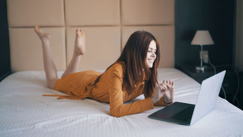 Young woman using laptop while lying on bed at home