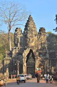 People and vehicles on street leading towards bayon temple against sky