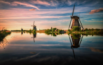 Traditional windmill by lake against sky during sunset