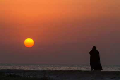 Silhouette woman standing at beach against sky during sunset