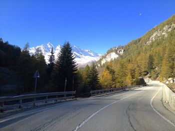 Road by trees against clear blue sky