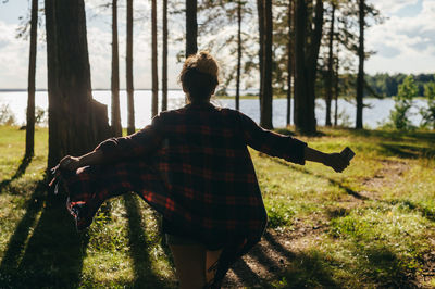 Rear view of man standing on field against trees in forest