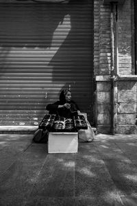 Woman selling sunglasses while sitting on footpath against closed shutter