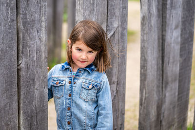 Portrait of smiling girl standing by plank outdoors