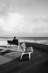 Man sitting on bench looking at sea against sky