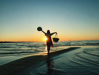 Silhouette woman standing at beach against sky during sunset