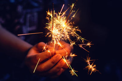 Midsection of person holding illuminated sparklers at night