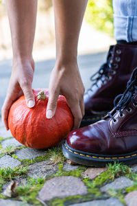 Vertical close up of hands and boots of a young woman, who lifts up an orange pumpkin.