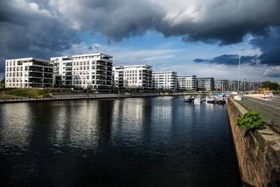 Buildings by river against sky in city