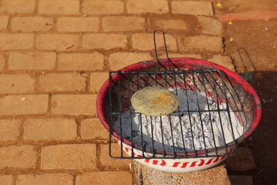 High angle view of food on barbecue grill with ash in container over footpath