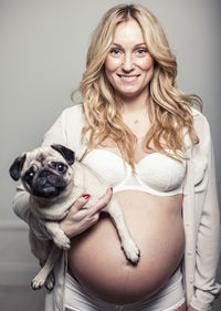 Portrait of happy pregnant woman holding pug dog at home