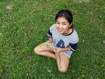 Portrait of smiling young woman holding plant while sitting on grassy field