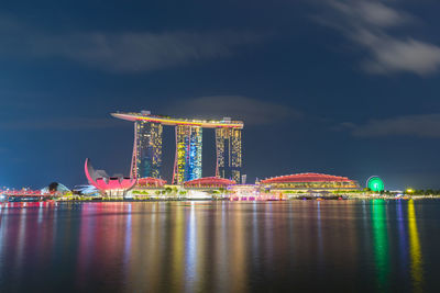 Illuminated city by sea against sky at night