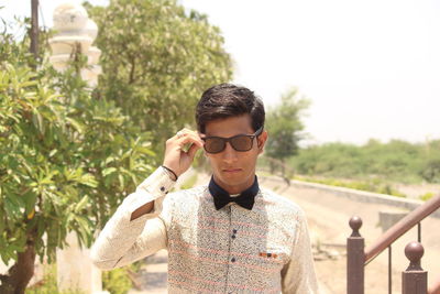 Portrait of young man wearing sunglasses standing against plants