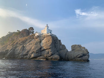 Lighthouse on rock by sea against sky