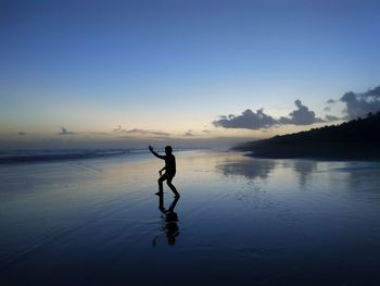 Silhouette man on sea against sky during sunset