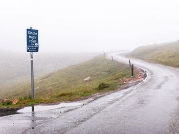 Road sign on roadside against sky