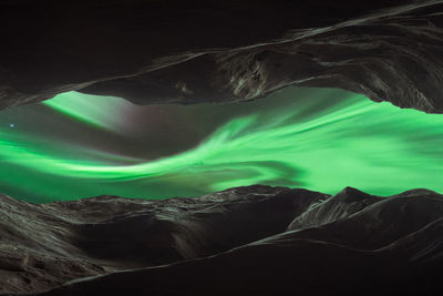 Through hole in rocky mountains view of dark night sky with glowing green polar lights in norway