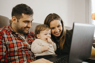 Happy mother and father with son during video call on laptop sitting in living room