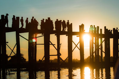 Silhouette people on lake against sky during sunset