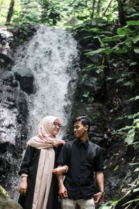 Smiling couple standing arm in arm against waterfall