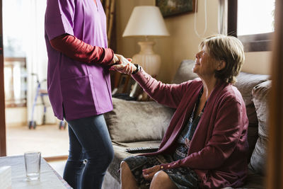 Healthcare worker holding hands with senior woman in living room