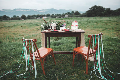 Empty chairs by table on field against sky