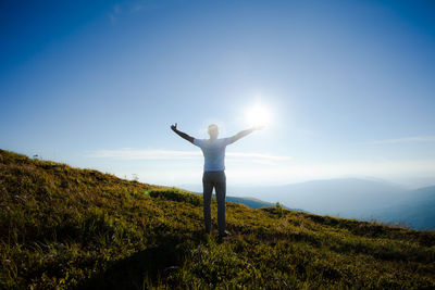 Rear view of man with arms outstretched standing on field against sky