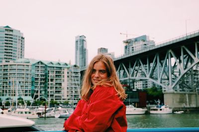 Side view portrait of young woman standing against bridge in city