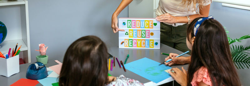 Teacher explaining to students a ecologic process using lightbox with text reduce, reuse, recycle