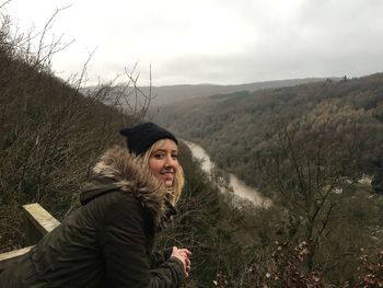 Portrait of young woman leaning on railing against landscape during winter