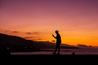 Silhouette person using mobile phone at beach during sunset