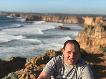 High angle portrait of man standing on cliff by sea against sky